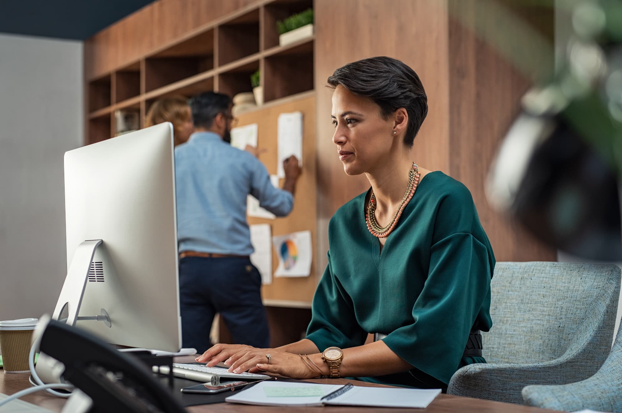Analyst at a desktop screen while colleagues pin notes to a board